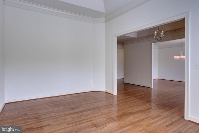 unfurnished room with a chandelier, light wood-style floors, ornamental molding, and baseboards
