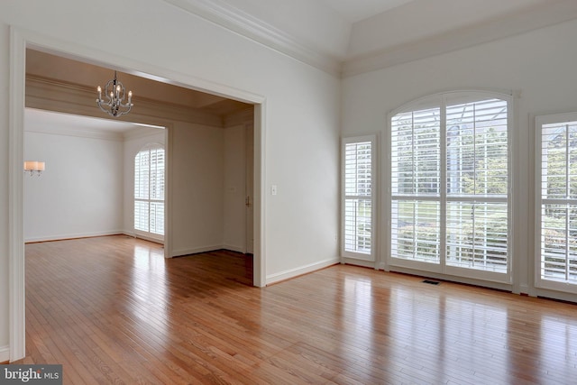 unfurnished room with a chandelier, plenty of natural light, light wood-style flooring, baseboards, and crown molding