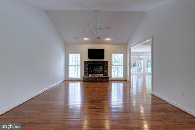 unfurnished living room featuring ceiling fan, a stone fireplace, hardwood / wood-style flooring, baseboards, and high vaulted ceiling