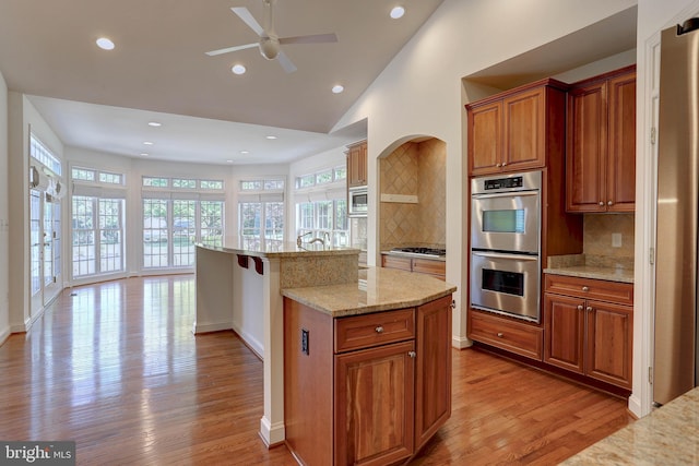 kitchen with stainless steel appliances, light wood finished floors, ceiling fan, decorative backsplash, and recessed lighting
