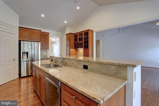 kitchen featuring appliances with stainless steel finishes, a sink, lofted ceiling, light wood-style flooring, and backsplash