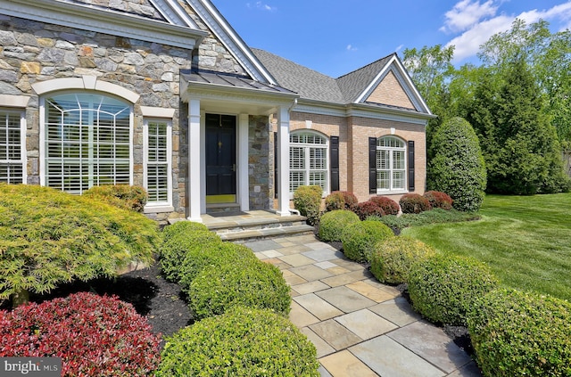 doorway to property with a standing seam roof, stone siding, and a lawn
