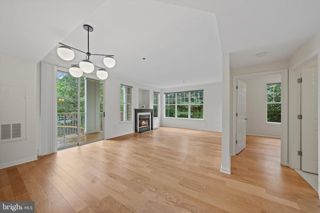 unfurnished living room featuring healthy amount of natural light, light wood-type flooring, a chandelier, and a warm lit fireplace