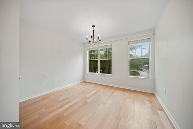unfurnished room featuring a chandelier, light wood-style flooring, and baseboards