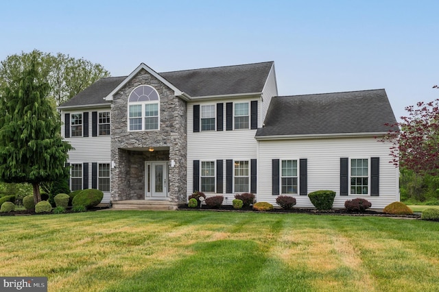 colonial home with a shingled roof, stone siding, and a front yard
