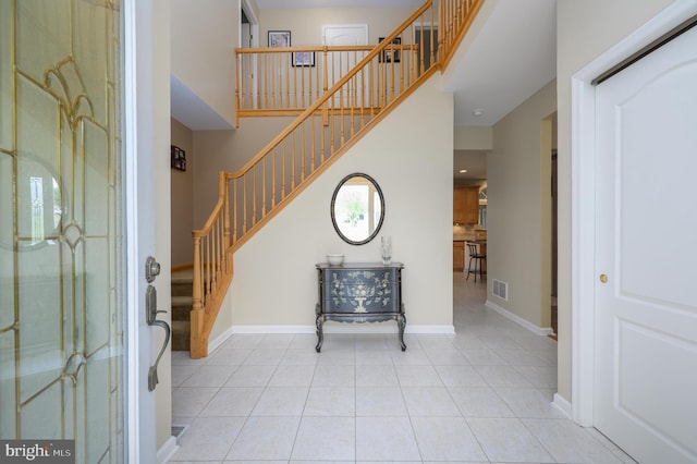 foyer with stairs, light tile patterned flooring, visible vents, and a high ceiling