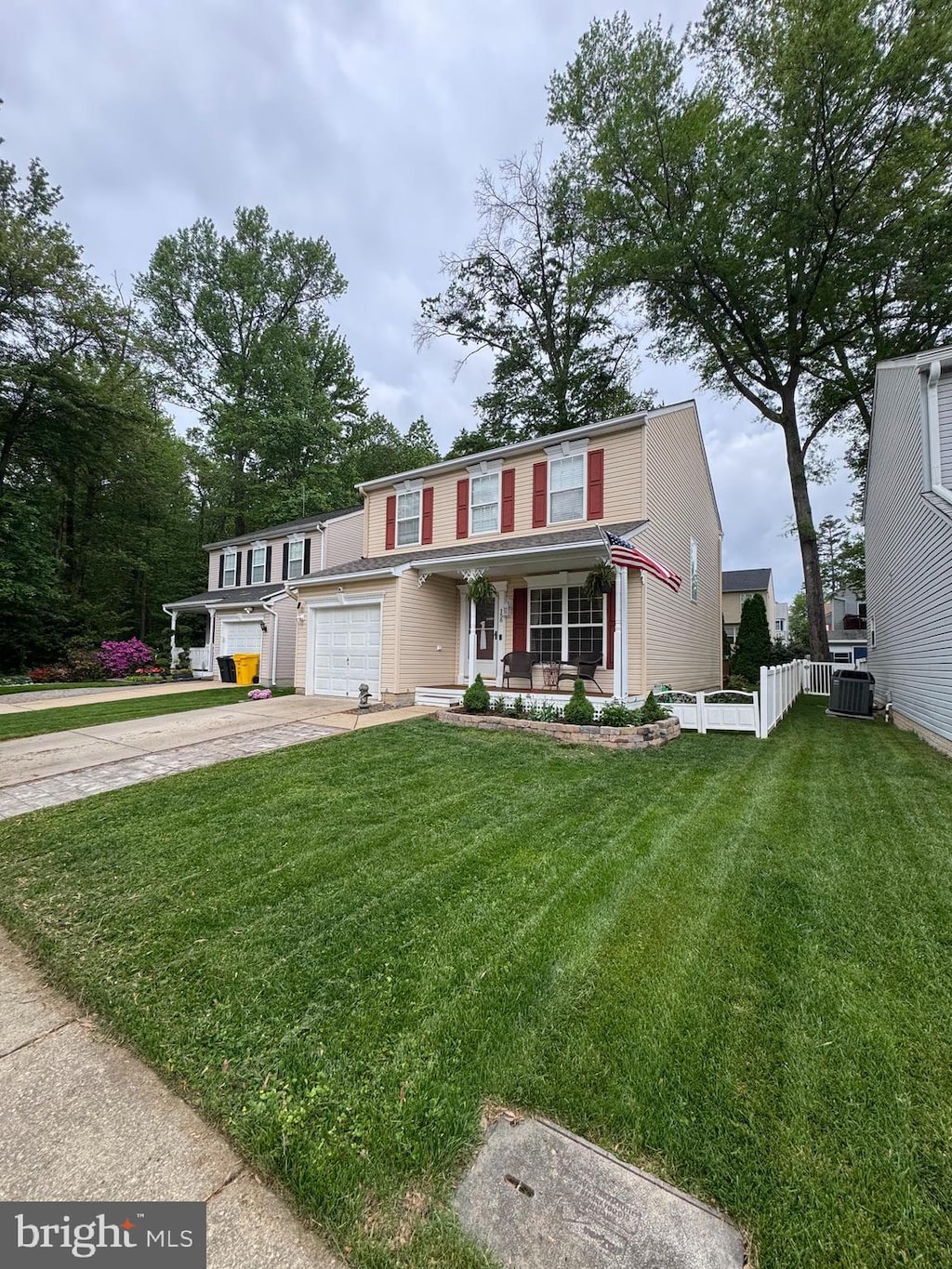 view of front facade featuring covered porch, fence, a front lawn, central AC unit, and driveway