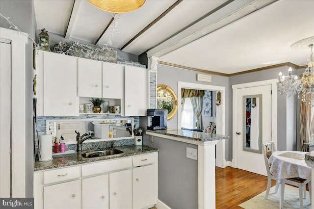 kitchen with a sink, wood finished floors, dark stone counters, an inviting chandelier, and white cabinets