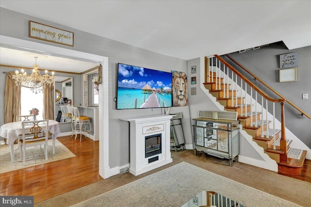 living area with an inviting chandelier, wood finished floors, baseboards, a glass covered fireplace, and stairs