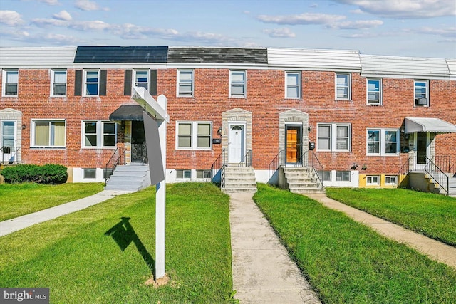 view of property featuring entry steps, a front lawn, and brick siding