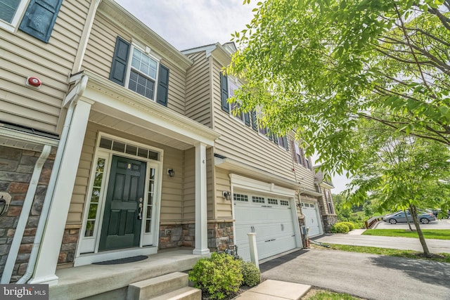 view of exterior entry with an attached garage, stone siding, asphalt driveway, and covered porch