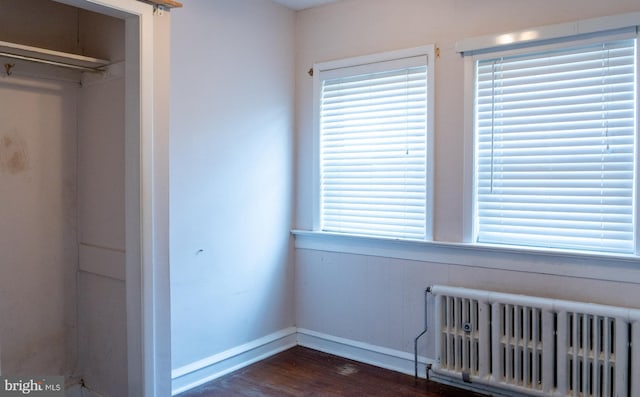 unfurnished bedroom featuring baseboards, radiator heating unit, a closet, and dark wood-style floors