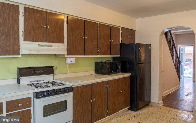 kitchen with light floors, under cabinet range hood, arched walkways, black appliances, and light countertops