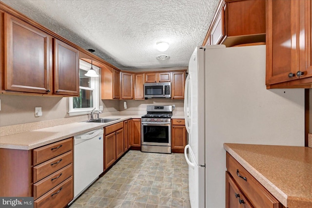 kitchen with appliances with stainless steel finishes, a sink, brown cabinetry, light countertops, and a textured ceiling