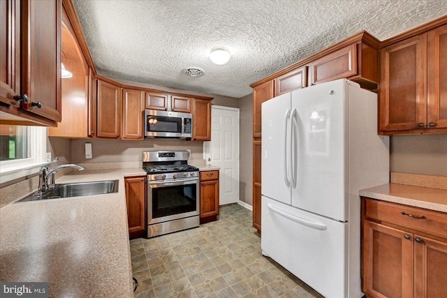 kitchen featuring appliances with stainless steel finishes, a sink, brown cabinets, light countertops, and a textured ceiling