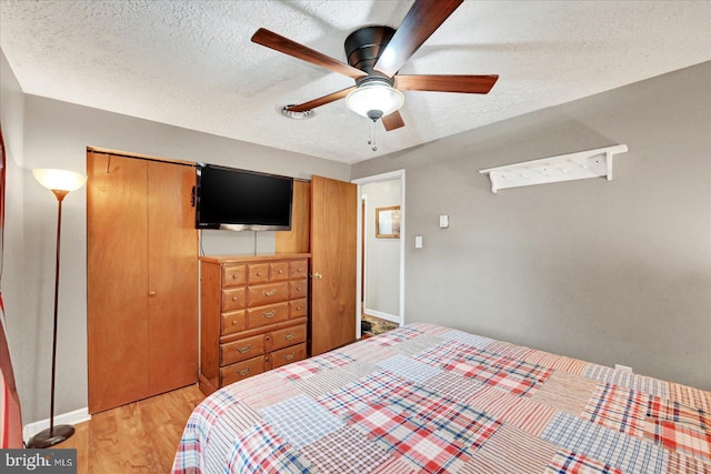 bedroom featuring light wood-style floors, a closet, baseboards, a textured ceiling, and a ceiling fan
