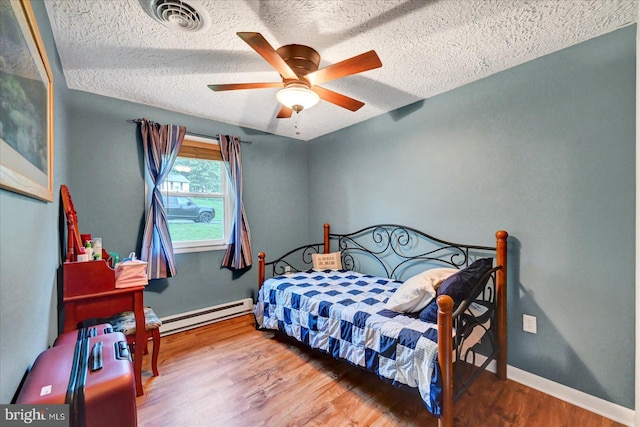 bedroom with baseboard heating, wood finished floors, a textured ceiling, baseboards, and ceiling fan