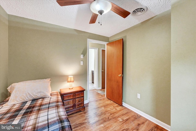 bedroom with wood finished floors, a textured ceiling, baseboards, and a ceiling fan