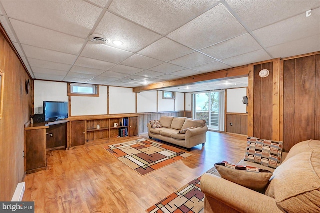 living area with wood finished floors, wood walls, plenty of natural light, and a drop ceiling