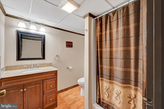 full bathroom with wood finished floors, vanity, toilet, a drop ceiling, and baseboards