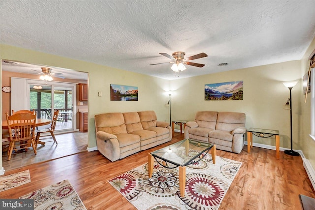 living room with ceiling fan, light wood-type flooring, a textured ceiling, and baseboards