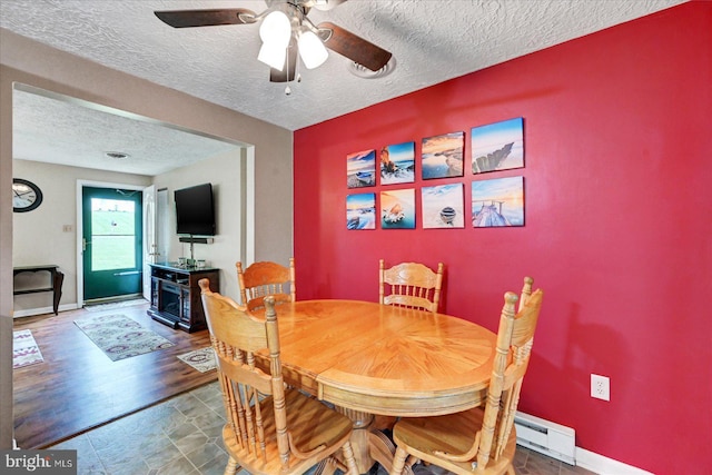 dining area featuring a baseboard heating unit, a textured ceiling, ceiling fan, and baseboards