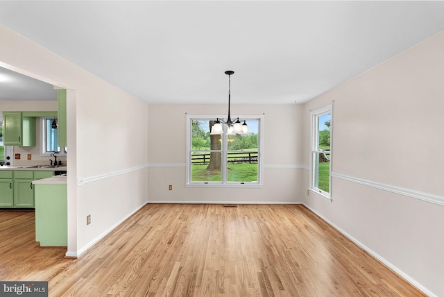 unfurnished dining area with light wood finished floors, baseboards, a chandelier, and a sink