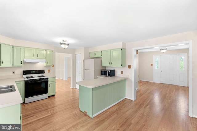kitchen featuring range with gas stovetop, green cabinetry, under cabinet range hood, and freestanding refrigerator