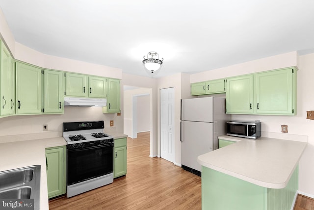 kitchen with gas stove, stainless steel microwave, under cabinet range hood, freestanding refrigerator, and a sink