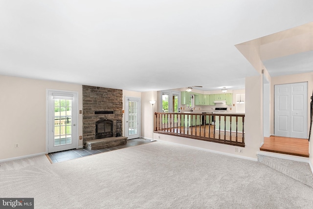 unfurnished living room with carpet flooring, baseboards, a fireplace, a sink, and a ceiling fan