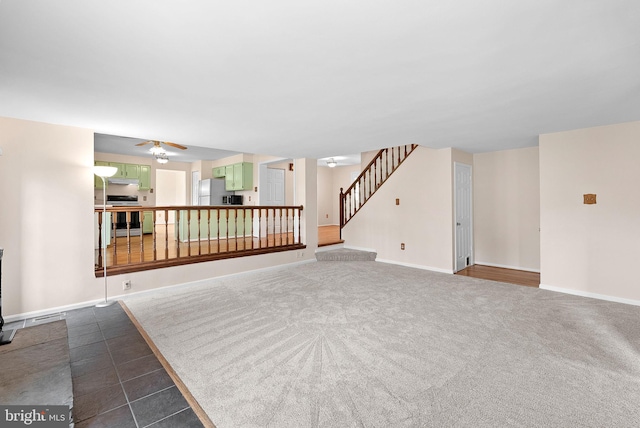 unfurnished living room featuring stairway, baseboards, ceiling fan, and dark colored carpet