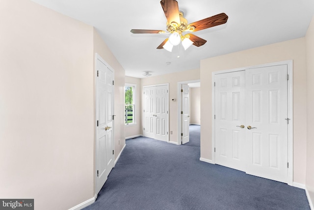 unfurnished bedroom featuring multiple closets, dark carpet, baseboards, and a ceiling fan