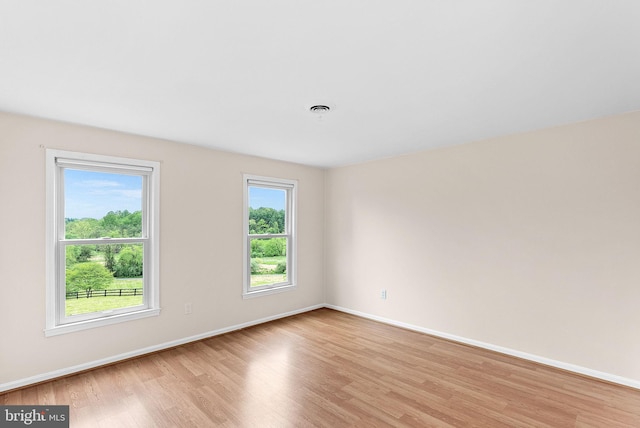unfurnished room featuring light wood finished floors, plenty of natural light, and baseboards