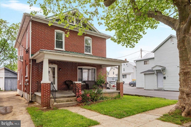 american foursquare style home featuring covered porch, brick siding, an outdoor structure, and a front yard