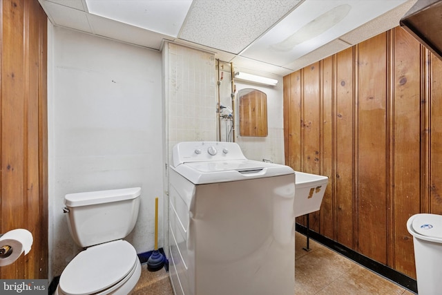 bathroom with washer / dryer, toilet, a paneled ceiling, and wood walls