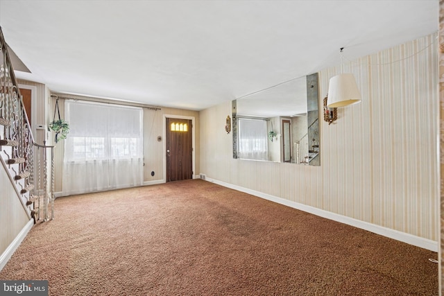 unfurnished living room with stairs, carpet, and baseboards