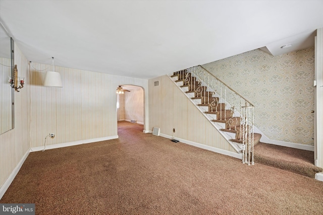 basement with wallpapered walls, carpet, stairway, arched walkways, and baseboards