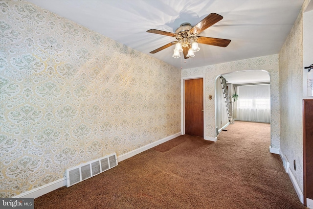 unfurnished room with wallpapered walls, carpet floors, ceiling fan, arched walkways, and baseboards