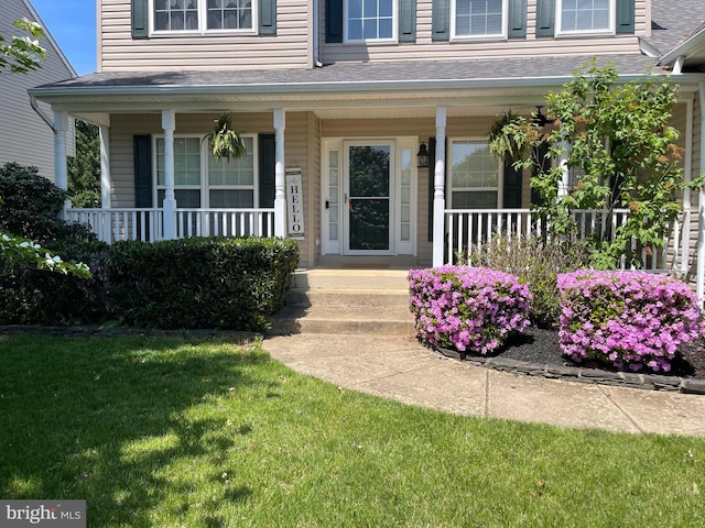 entrance to property with covered porch, a shingled roof, and a lawn