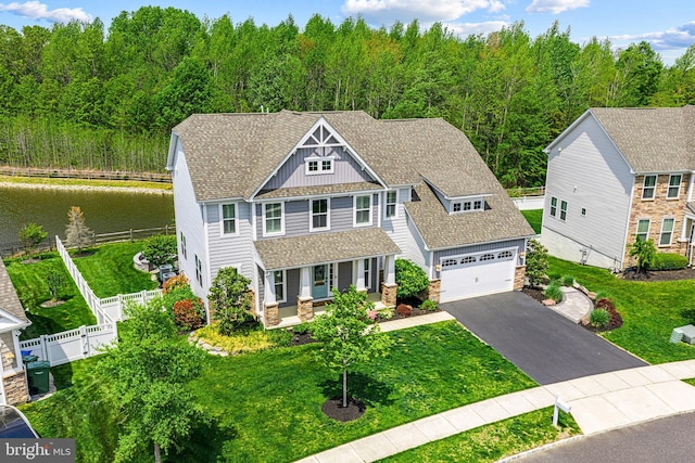 shingle-style home featuring stone siding, covered porch, a water view, fence, and aphalt driveway