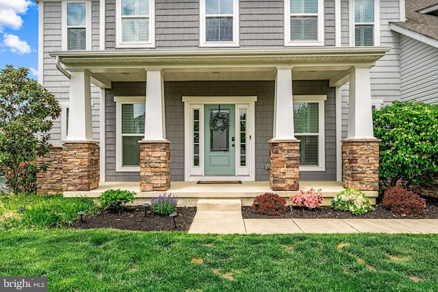 view of exterior entry featuring a porch, a yard, and stone siding