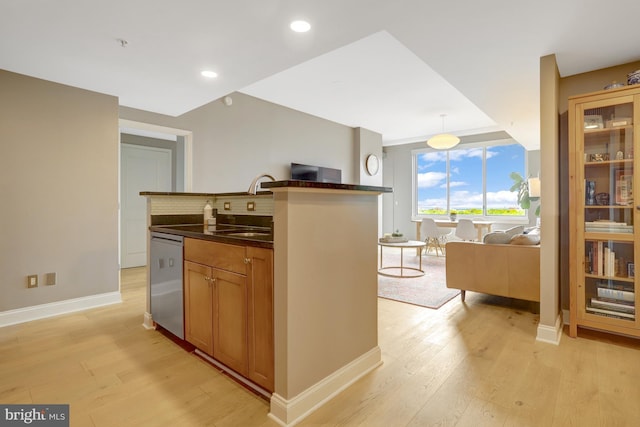 kitchen with dishwasher, light wood-style flooring, open floor plan, dark countertops, and a sink