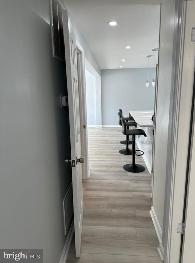 hallway featuring light wood-style floors, visible vents, baseboards, and recessed lighting