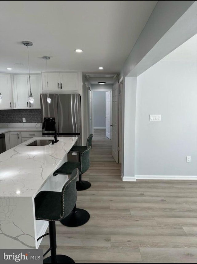 kitchen featuring a sink, freestanding refrigerator, white cabinetry, and baseboards