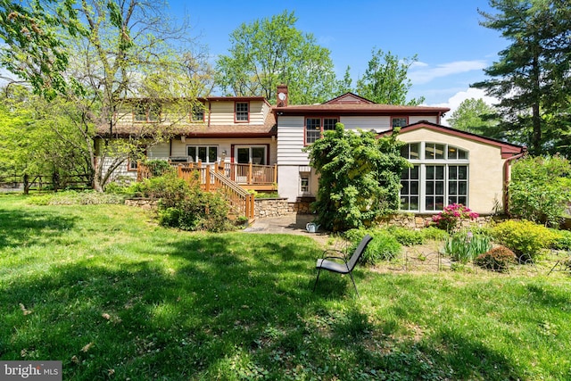 rear view of property with a chimney, a wooden deck, a lawn, and stairs