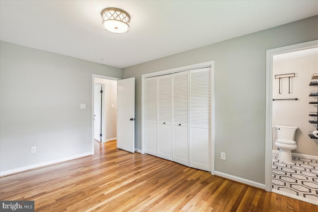 unfurnished bedroom with baseboards, ensuite bathroom, light wood-style floors, and a closet