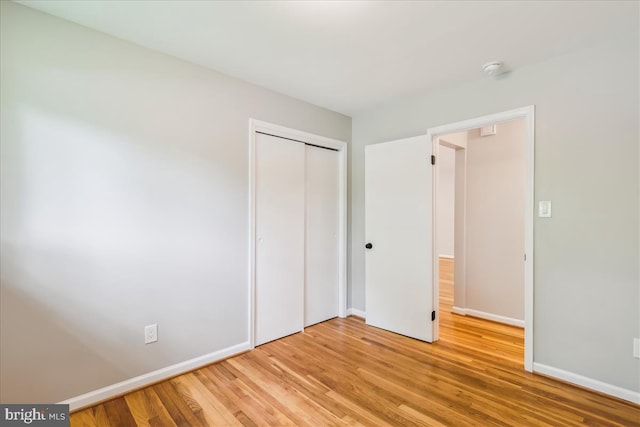 unfurnished bedroom featuring light wood-style flooring, a closet, and baseboards