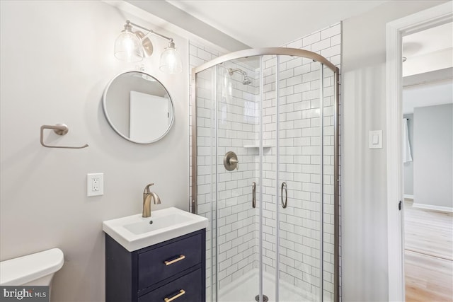 full bath featuring a stall shower, vanity, toilet, and wood finished floors