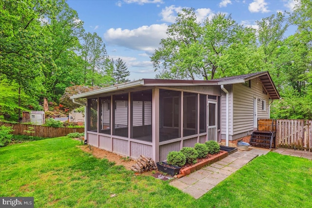 rear view of house with a sunroom, fence, and a lawn