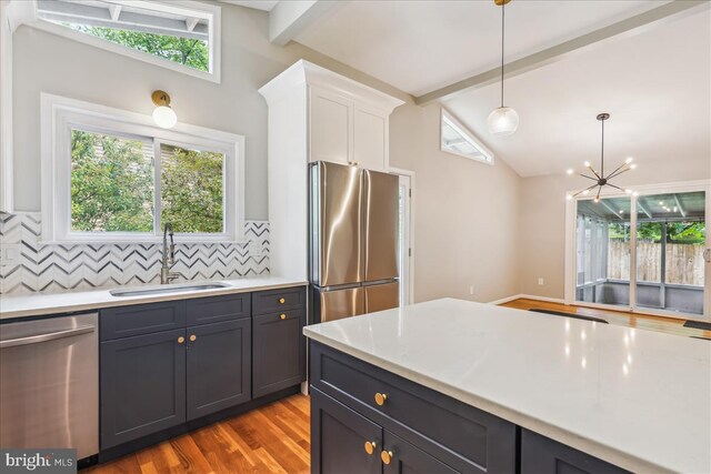 kitchen with a sink, stainless steel appliances, lofted ceiling with beams, white cabinetry, and tasteful backsplash